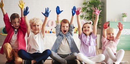 Roześmiane dzieci z uniesionymi pomalowanymi na kolorowo dłońmi
