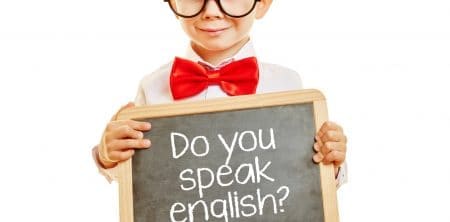 Elegancko ubrane dziecko trzyma w dłoniach tablicę z napisem "Do you speak English?"