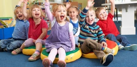 Uśmiechnięte dzieci w przedszkolu podnoszą ręce do góry